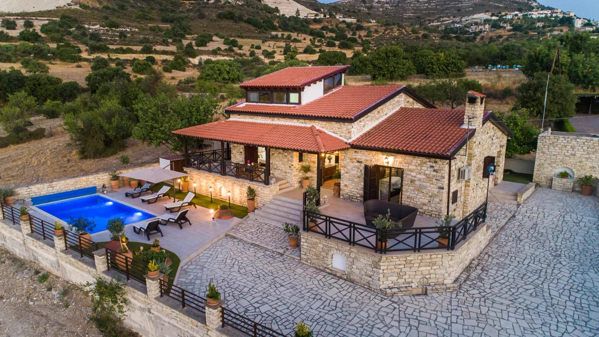 Stone villa, terraces and lit pool at dusk